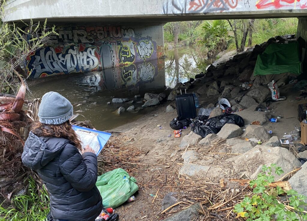 Census Documenting Hand Built Structure A volunteer documents an area along the river where people experiencing homelessness have been living.