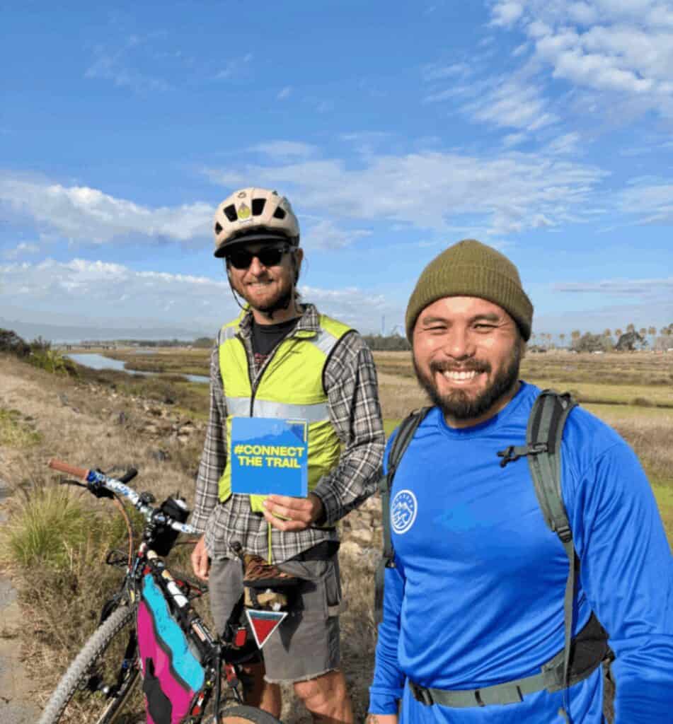 one mail biker and one person smiling at the camera on the san diego river trail path