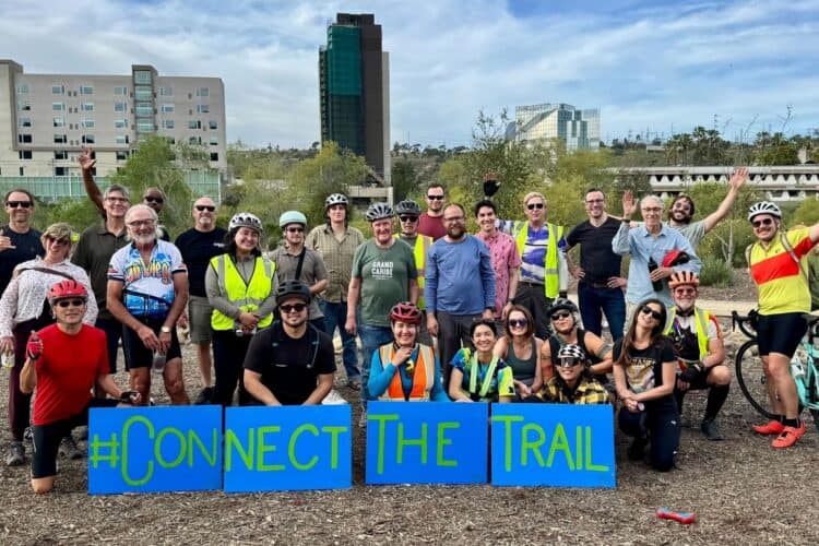 group of River Action Trail volunteers on their bikes and standing in front of a sign that says Connect the Trail