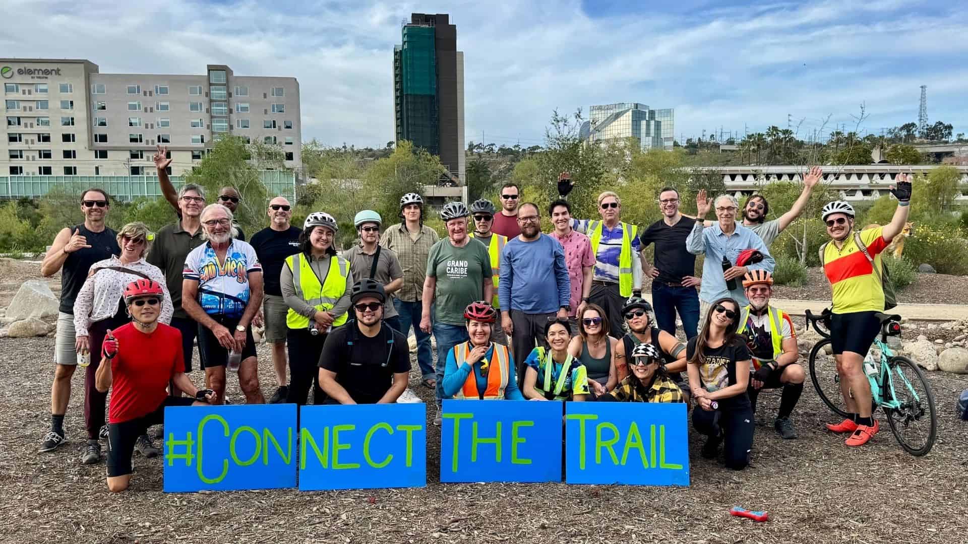 group of River Action Trail volunteers on their bikes and standing in front of a sign that says Connect the Trail