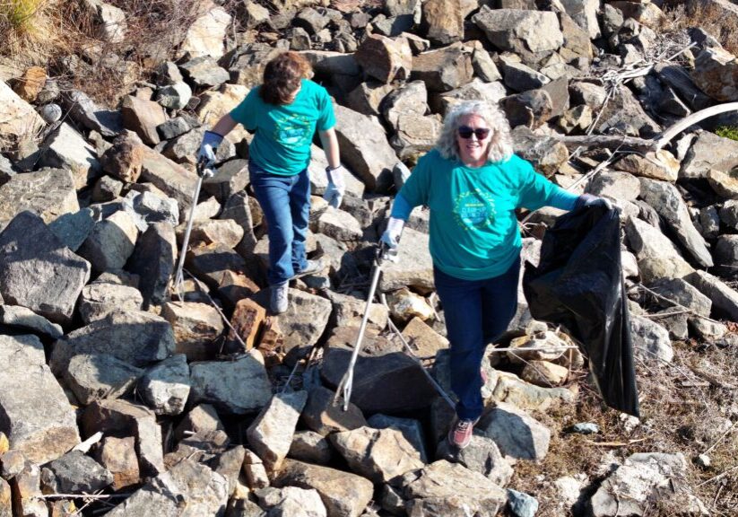 Two volunteers pick up trash along the banks of the San Diego River