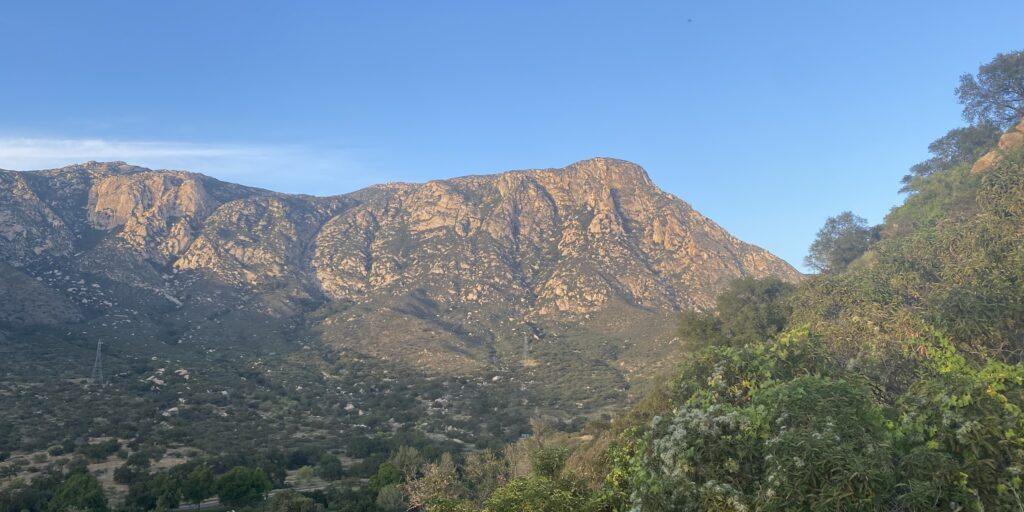 The face of El Cajon Mountain set against a blue sky, with green trees in the foreground.