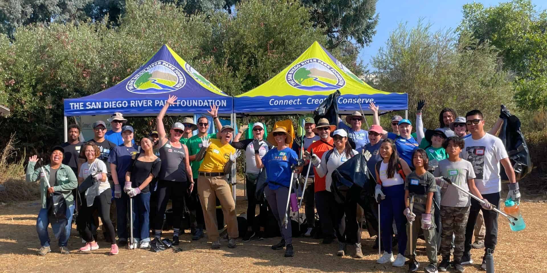 group of volunteers at a cleanup waiving trash pickers and smiling