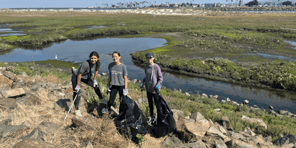 Three women pose in front of the estuary during a trash clean up event